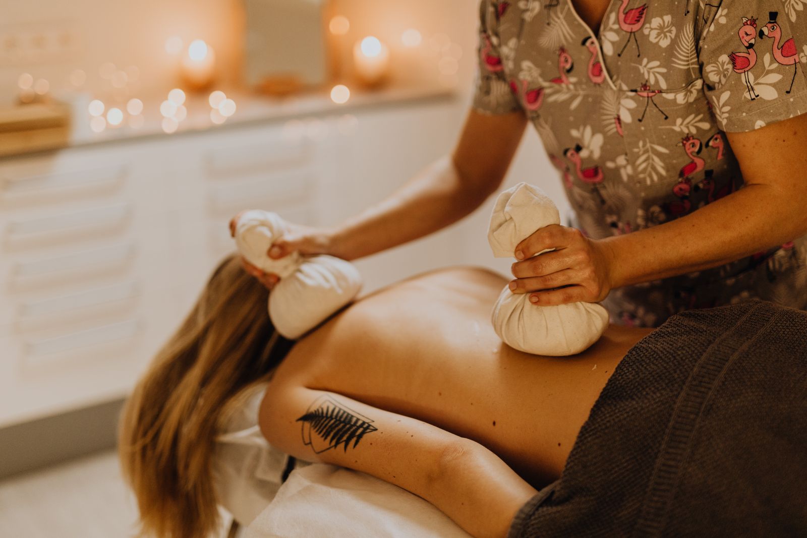 Therapist pressing warm herbal compresses along a guest's back